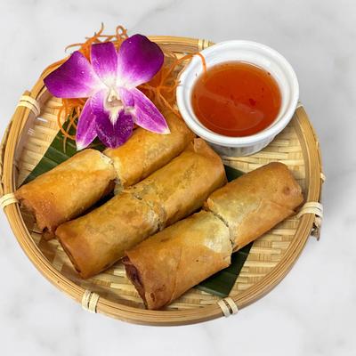 Four golden fried spring rolls served with dipping sauce in a basket.
