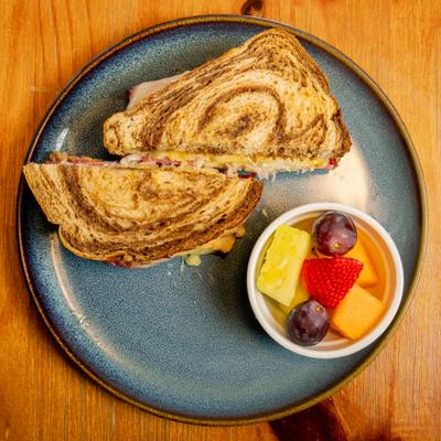 The Rueben sandwich with a fruit bowl on the side.
