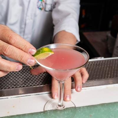 Cosmopolitan in martini glass, being garnished with a lime wedge.
