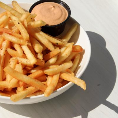 French fries served in a white bowl with a dip on the side.