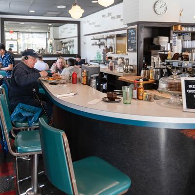 A  diner with teal stools and a curved counter, Patrons enjoying meals.