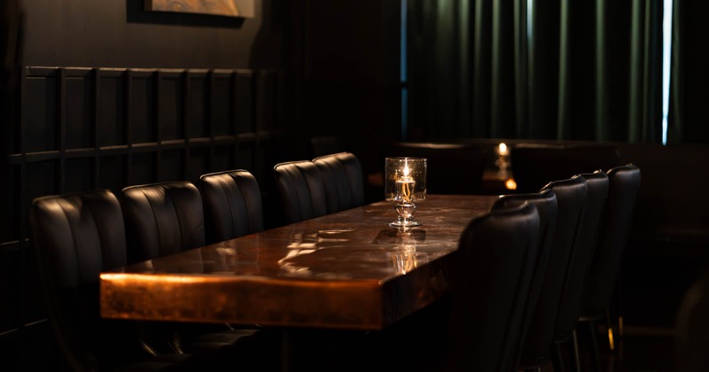 Interior, dining room, long polished wooden table, dark chairs, and candles casting warm reflections