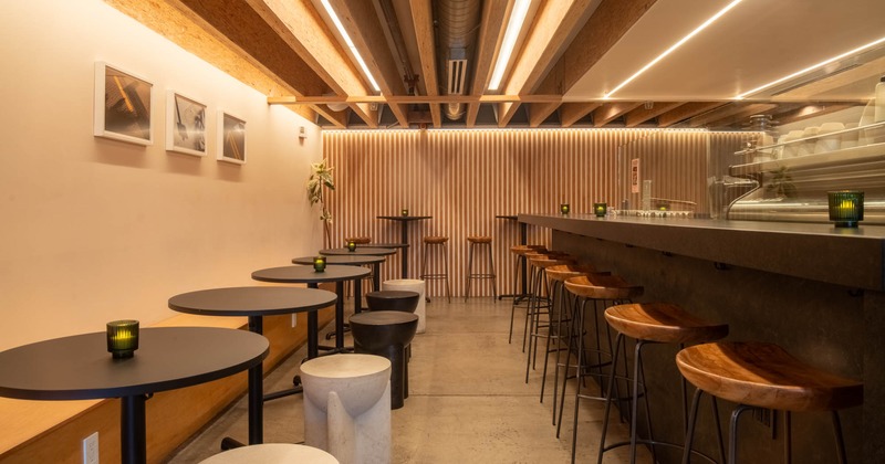 Modern cafe interior with round tables, stools, a long bar, and warm lighting