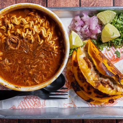 Birria ramen noodles served with two quesabirria tacos.