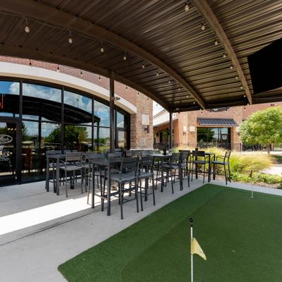 Outdoor seating covered by a pergola with string lighting and a small putting green.