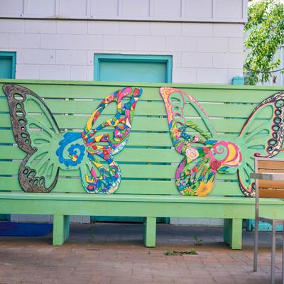 Patio details, colorful butterfly art on green bench beside an outdoor seating area.