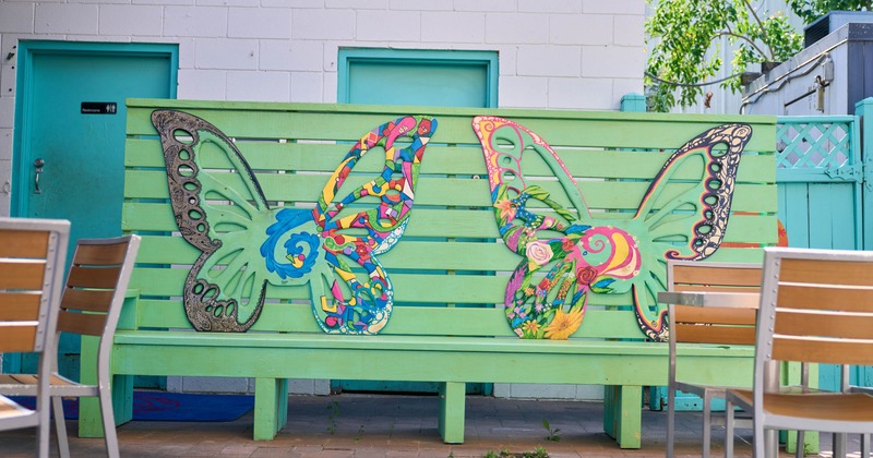 Patio details, colorful butterfly art on green bench beside an outdoor seating area