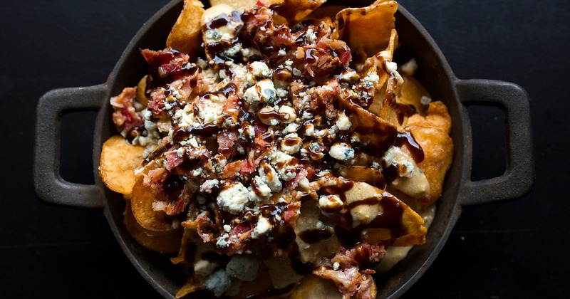 Loaded nachos served in a rustic metal pan on a dark background