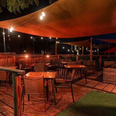 Outdoor patio featuring wooden tables, chairs, string lights, and orange shade sails.