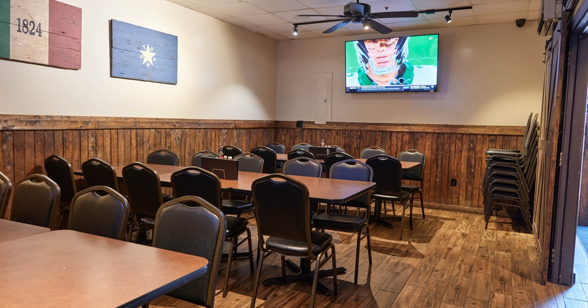 Seating room featuring long tables with chairs, a tv screen, flags of Alamo and Texas