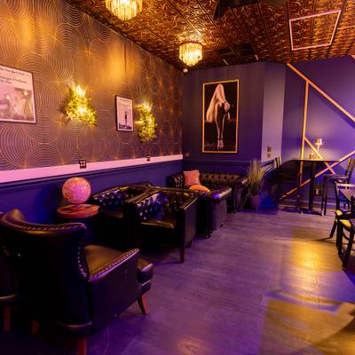 Dimly lit cocktail bar interior featuring tufted black leather seating.