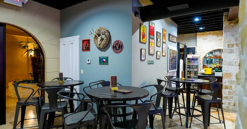 Interior of a dining area with high tables, black chairs, wall art, and a view into a bar area