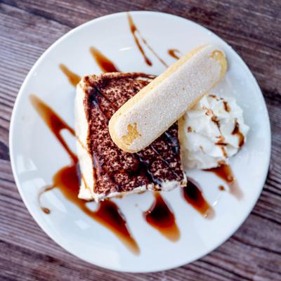 A piece of tiramisu topped with a ladyfinger biscuit and whipped cream.