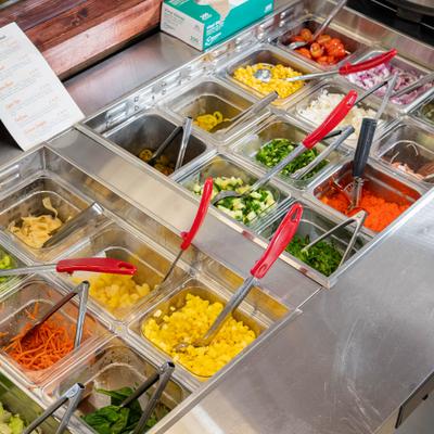 Salad bar with assorted toppings in metal containers.