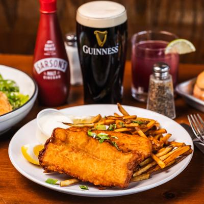 Fish & Chips plate on a wooden table with other dishes, dark beer and a red cocktail.