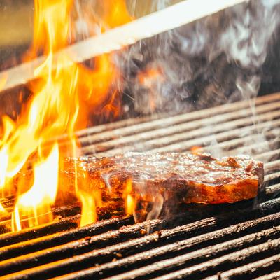 Steak grilling over open flames with smoke rising.