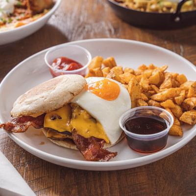 Breakfast burger topped with bacon and a fried egg, served with potatoes and dipping sauces