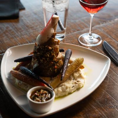 Lamb shank with glazed carrots and mashed potatoes served with red wine.