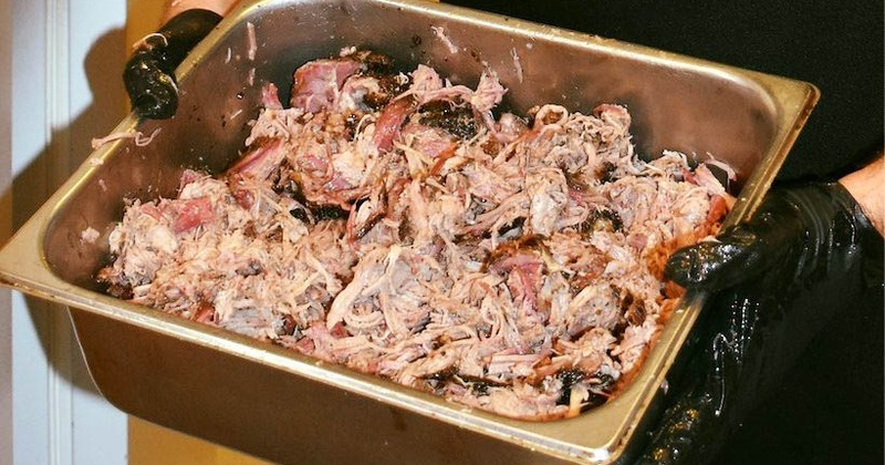 Pulled pork in a large container held by hands