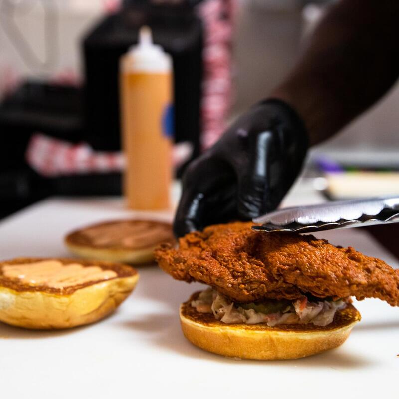 Staff member in gloves preparing a chicken burger