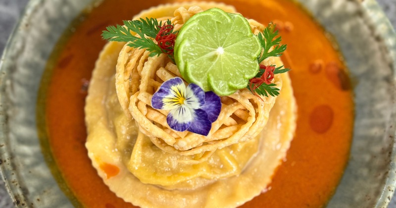 Thai coconut curry noodle soup garnished with flowers and carved lime