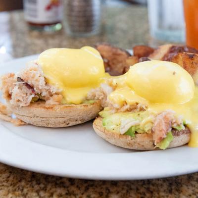 Dungeness crab eggs Benedict with hollandaise sauce, avocado, and a side of potatoes.