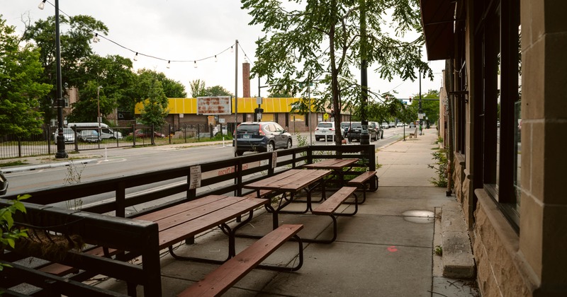 Outdoor seating area with wooden tables and benches along a sidewalk