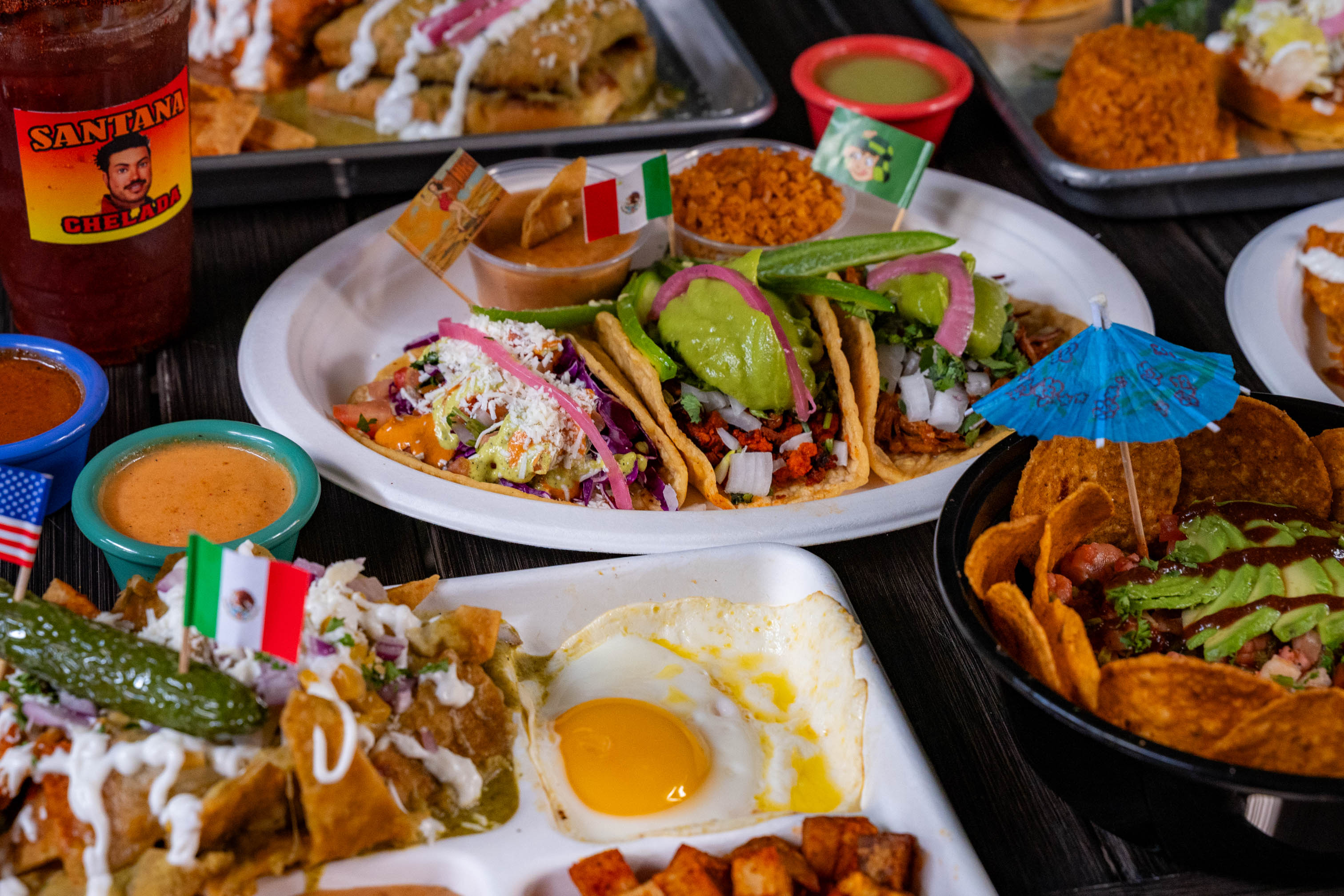 Assorted dishes spread on a table with dishes such as a trio of tacos, chilaquiles and sides