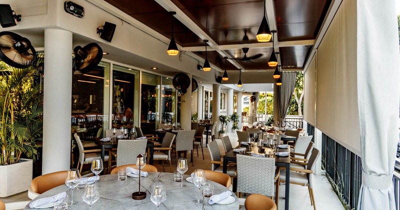 Outdoor dining area with tables and chairs set for service, glass windows, pendant lights