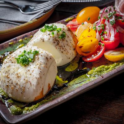 Burrata and prosciutto board with tomatoes and herbs.