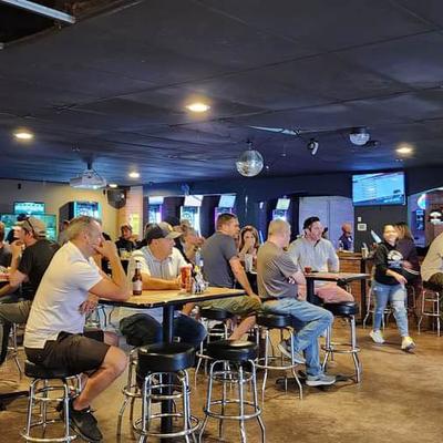 A lively bar scene with people sitting at tables, watching TV, and enjoying drinks.