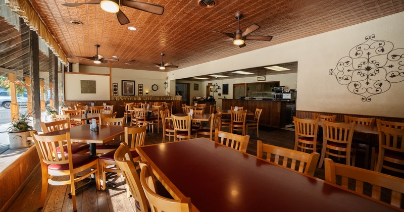 Interior of a restaurant with wooden tables and chairs, textured copper ceiling, and natural light