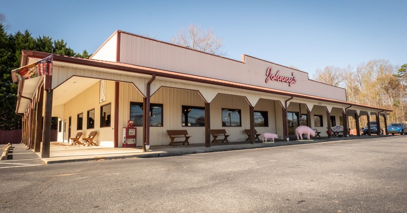 A front view to the restaurant,  terrace, seating area, tables, sign, piglet figure