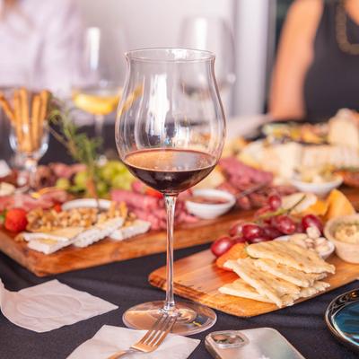 A glass of red wine with charcuterie board behind it.