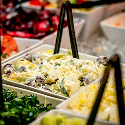 Various salad bar dishes are displayed in white containers with black tongs.