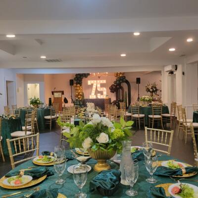 An elegant room decorated for a seventy-fifth birthday featuring green tables and balloons.