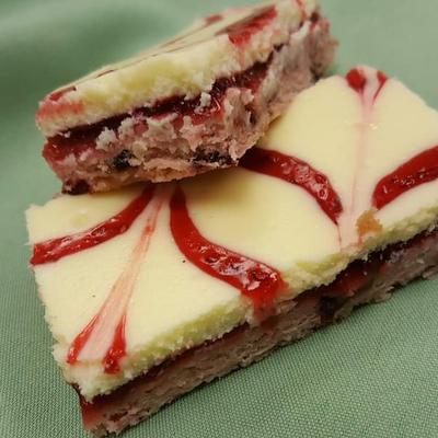Two layered cheesecake bars with creamy top and red swirl patterns.