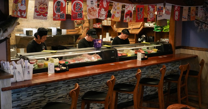 Cozy sushi bar with three chefs preparing dishes behind a counter