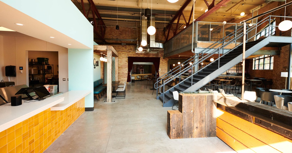 Modern industrial bar with mezzanine seating, yellow counter, and pendant lights