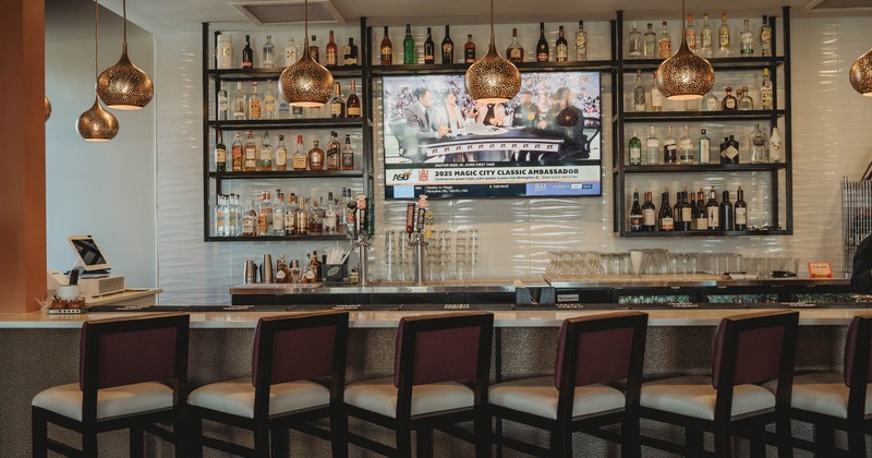 A modern bar with a countertop, high-backed chairs, liquor shelves, a TV