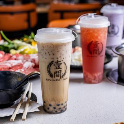 Three plastic cups with bubble tea lined on the table alongside various dishes.
