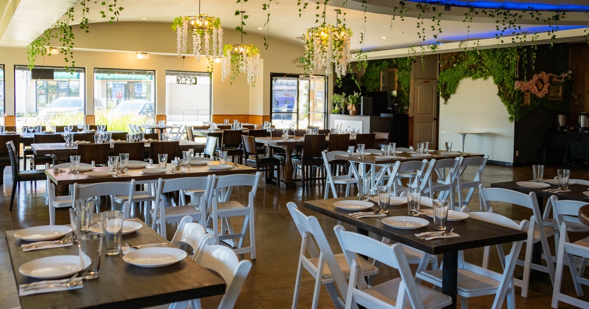 iInterior with tables set for dining, decorated with hanging flowers and greenery