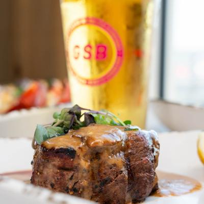 Seared filet mignon with creamy sauce, fresh garnish, and a tall beer.