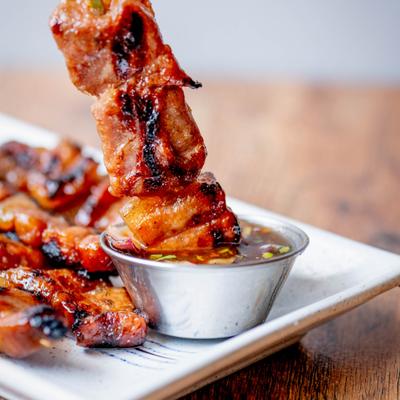 Grilled pork skewers being dipped into sauce.