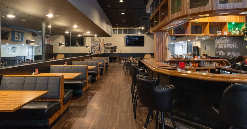 Modern bar interior with wooden booths lining the left, a bar with cushioned stools on the right