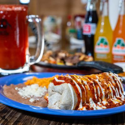 Burrito topped with chili sauce and sour cream, served with rice and refried beans.