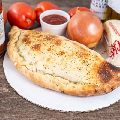 Cheese calzone surrounded by fresh tomatoes, an onion, marinara sauce, and cheese.