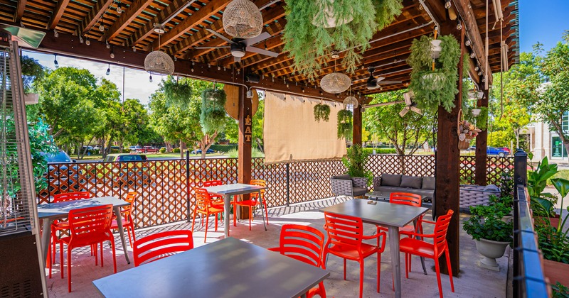 Outdoor restaurant patio with red chairs, gray tables, hanging plants, lights, ceiling fans
