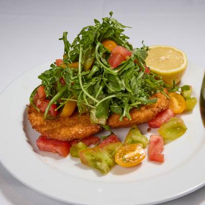 Chicken Milanese topped with arugula and tomato salad.