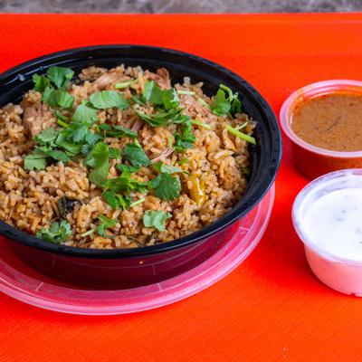 Biryani served in a black bowl, accompanied with two small containers of sauces.